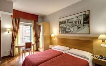 Hotel Rio twin bedroom with red bedspreads, wooden furniture, a desk by the window, and a large black and white wall photo