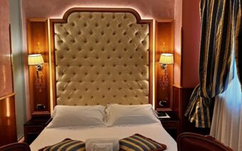 A bed with tufted headboard flanked by wall lamps and wood paneling in a Hotel Vittoria guest room