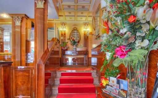 Hotel Vittoria interior featuring red carpeted stairs, wooden walls, a mirror, and a large floral arrangement