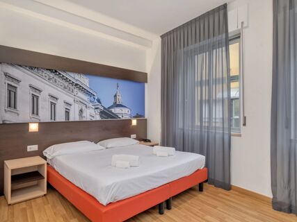 Double bed with white linens and two pillows under wooden panel with a framed photo at B&B Hotel Milano Ornato