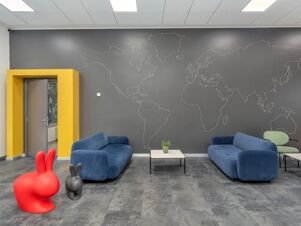 Lobby area of B&B Hotel Milano Ornato with blue sofas, a small marble table with a plant, and a world map on the wall