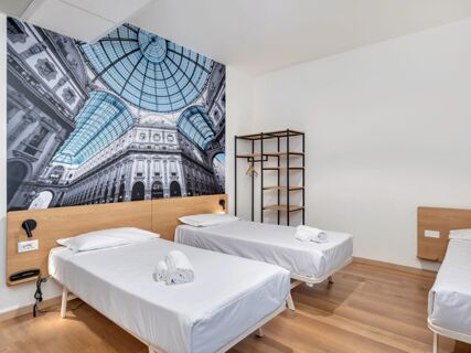 Two single beds with white linens and wooden headboards under a black and white architectural wall mural at B&B Hotel Milano Ornato with a black rack nearby