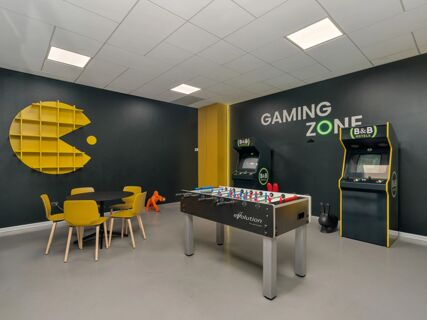 Gaming zone room at B&B Hotel Milano Ornato with foosball table, arcade machines, yellow chairs, and round table visible