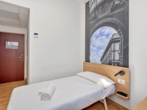 Single bed with white linens and towels, wooden headboard, wall art of archway and building, at B&B Hotel Milano Ornato