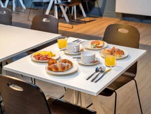 Breakfast table at B&B Hotel Milano Ornato with plates of croissants, sausages, scrambled eggs, juice glasses, coffee cups, and cutlery