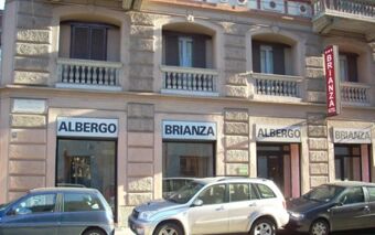 The exterior view of Hotel Brianza located in a stone building with multiple windows and cars parked in front of it