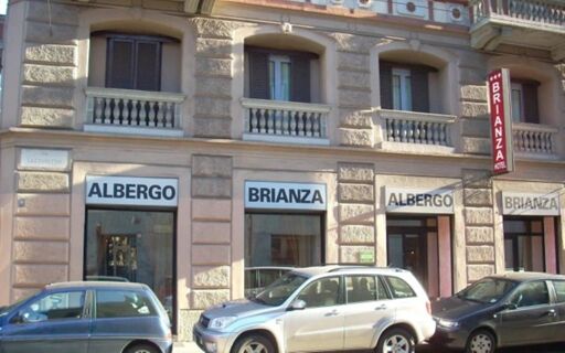 The exterior view of Hotel Brianza located in a stone building with multiple windows and cars parked in front of it
