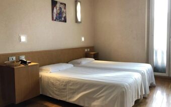 Two single beds with white linens are placed side by side in a room at Eurohotel Milan Hotel with wooden floors and simple wall decor