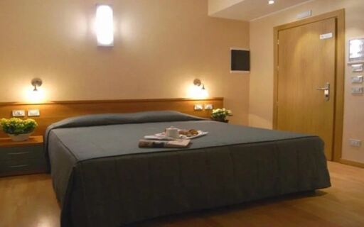 A simple hotel room at Eurohotel Milan Hotel with a gray bedspread, wooden floors, wall lights, and a wooden door in view