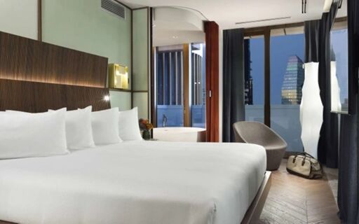 Spacious hotel room at Milano Verticale | UNA Esperienze with a large bed, armchair, city view, and modern bathroom visible through glass door