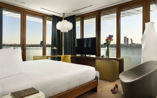 A modern hotel room at Milano Verticale | UNA Esperienze with a large bed, floor-to-ceiling windows, and city views visible outside