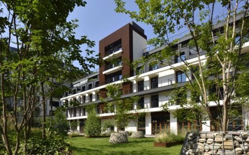 Modern multi-story white building with balconies surrounded by green trees and lawn at Milano Verticale | UNA Esperienze