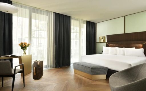 Spacious hotel room at Milano Verticale | UNA Esperienze with a large bed, seating area, wooden floor, and large windows with curtains