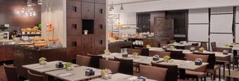 Dining area with multiple tables and chairs next to a buffet setup at NH Milano 2 hotel restaurant