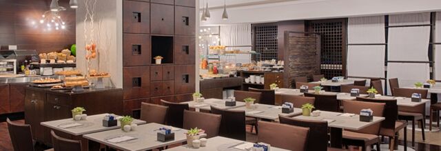 Dining area with multiple tables and chairs next to a buffet setup at NH Milano 2 hotel restaurant