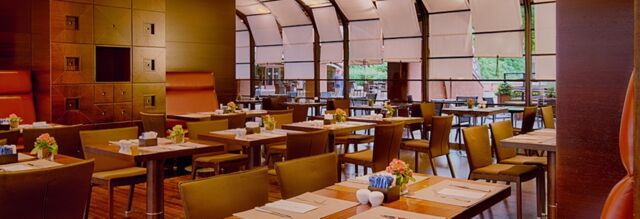 Dining area of NH Milano 2 with wooden tables, brown leather chairs, floral centerpieces, and large windows with blinds