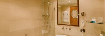 Bathroom with glass shower, wall-mounted hairdryer, towel rack, mirror, and sink at NH Milano 2 hotel