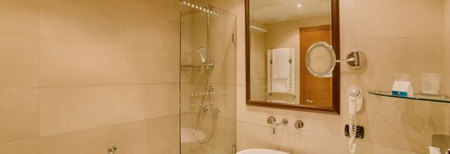 Bathroom with glass shower, wall-mounted hairdryer, towel rack, mirror, and sink at NH Milano 2 hotel
