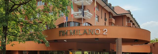 Orange building exterior with balconies and flags above the entrance showing the name NH Milano 2 in green and white letters