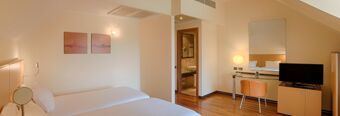 Hotel room at NH Milano 2 with two single beds, wooden floor, wall art, a desk with chair and TV on a cabinet