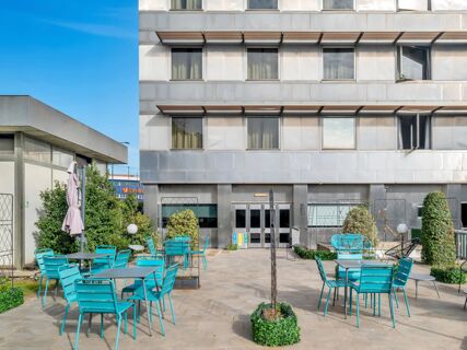 Outdoor seating area with turquoise chairs and tables in front of the gray modern facade of B&B Hotel Torino President building