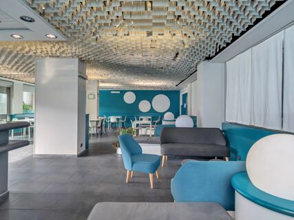 Spacious seating area with blue and gray chairs and sofas, white tables, and geometric ceiling at B&B Hotel Torino President