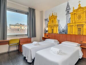 Two single beds with white linens and rolled towels in a room with a desk, chair, window, and mural at B&B Hotel Torino President