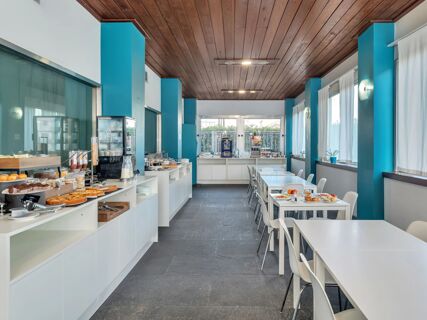 Breakfast area with white tables and chairs, buffet counters with pastries and cereal dispensers at B&B Hotel Torino President