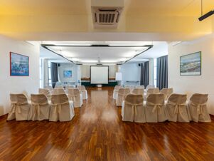 Conference room setup with rows of chairs covered in white fabric facing a projector screen at B&B Hotel Borgaro Torinese