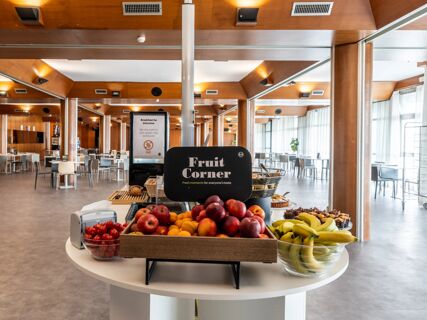 Fruit Corner display with apples, peaches, bananas, and cherry tomatoes inside a spacious dining area at B&B Hotel Borgaro Torinese