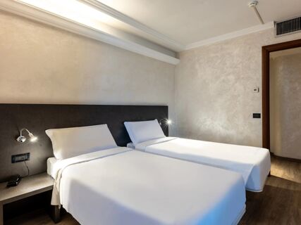 Two single beds with white linens and pillows in a minimalistic room at B&B Hotel Borgaro Torinese with bedside lamps and air vent