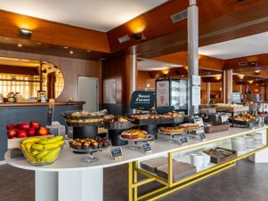 Buffet breakfast area at B&B Hotel Borgaro Torinese with various fresh fruits, pastries, breads, and signs on food items