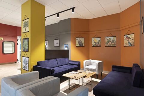 Seating area in B&B Hotel Como City Center with blue and white armchairs, coffee tables, and walls decorated with bird and plant paintings