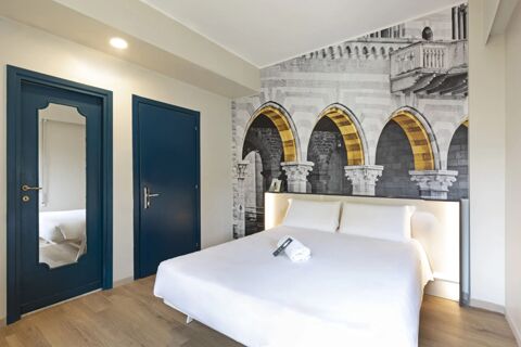 Modern hotel room at B&B Hotel Como City Center with a large bed, white bedding, wooden floor, and blue doors with a mirror