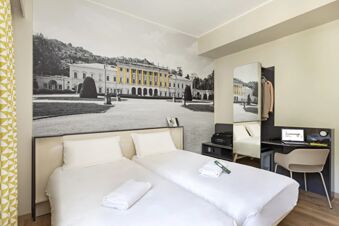 Twin beds with white linens and towels, a large black and white mural with yellow accents, and a desk area at B&B Hotel Como City Center