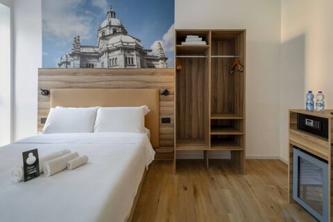 Double bed with white linens and towels next to wooden open wardrobe and minibar in B&B Hotel Como Baradello room