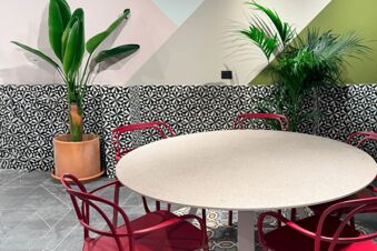 Round beige table with red chairs around it, two large green plants, and patterned wall tiles at B&B Hotel Como Baradello