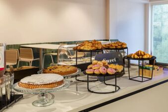 Various pastries including croissants, donuts, and cakes arranged on stands in a breakfast area at B&B Hotel Como Baradello