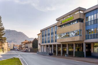 Modern beige and blue building with a green B&B Hotels sign on the facade along a quiet street near hills B&B Hotel Como Baradello