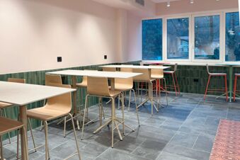Dining area with tables, wooden chairs, green tiled walls, large windows showing trees outside at B&B Hotel Como Baradello