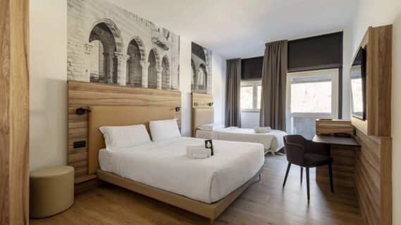 Hotel room at B&B Hotel Como Baradello with two beds, wooden accents, a TV, desk, chair, and large windows with curtains