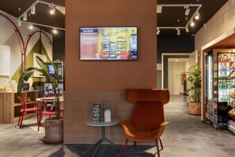 Interior lounge area with orange chair, potted plants, food vending machines, and a screen at B&B Hotel Como Baradello
