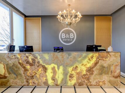 Lobby reception desk with yellow and brown marble, chandelier, gray wall with B&B Hotels logo at B&B Hotel Quarto D'Altino