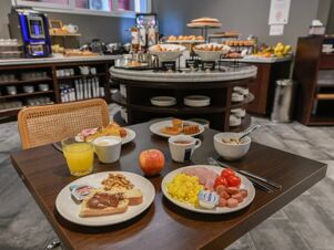 A breakfast spread with plates of scrambled eggs, ham, sausages, tomatoes, toast with Nutella, walnuts, orange juice, coffee, and an apple in the dining area of B&B Hotel Quarto D'Altino