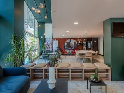 Modern seating area with blue couch, wooden benches with cushions, tables with plants, and a large window at B&B Hotel Firenze Centro
