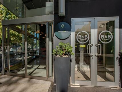 Glass entrance doors with B&B Hotels logos, a tall planter with green plant, and a welcome sign at B&B Hotel Firenze Centro
