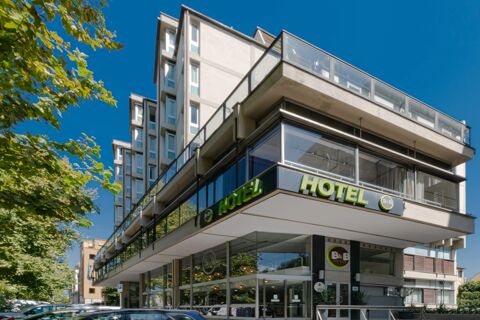 Modern multi-story building with glass windows and green signage for B&B Hotel Firenze Centro surrounded by trees and parked cars