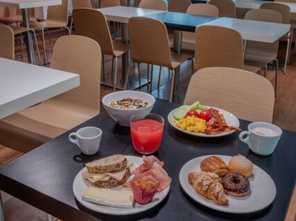 Breakfast with sandwiches, pastries, scrambled eggs, bacon, juice, coffee, and cereal served on a table inside B&B Hotel Firenze Centro