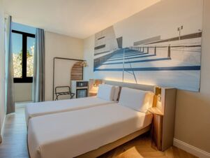 Two single beds with white linens under a large black and white wall art in a bright room at B&B Hotel Firenze Centro