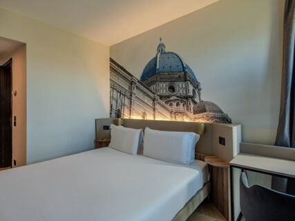 Minimalist hotel room at B&B Hotel Firenze Centro with a large bed, white pillows, mural of Florence dome, desk, and chair